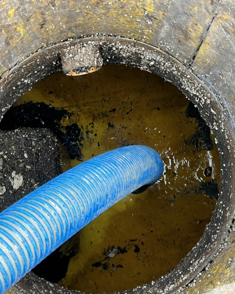 Blue suction hose lowered into an open drainage chamber